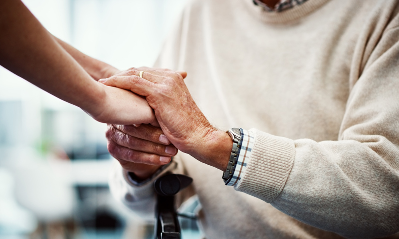 A man gently holding a woman's hand, with focus on their intertwined fingers and the detailing of his wristwatch. Their hands are showcasing well-groomed nails and visible veins.
