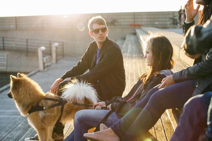A group of people sitting on a bench outdoors with a dog nearby.