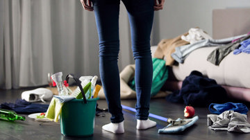 A woman with ADHD standing in a messy room with cleaning tools
