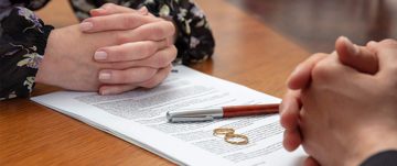 Couple discussing divorce with papers and rings on table.