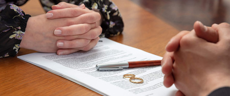 Couple discussing divorce with papers and rings on table.