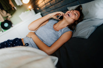 Woman chatting on phone in bed to a member of her migraine support group