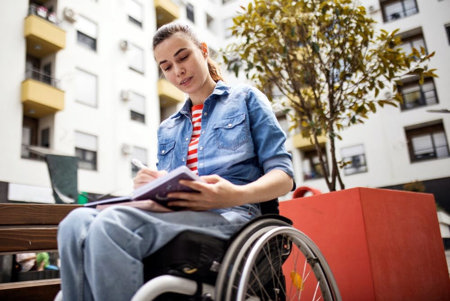 Woman sitting in wheelchair outside writing therapeutic poetry about migraine