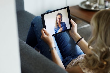 Woman on her sofa with a tablet, having her first online therapy session   