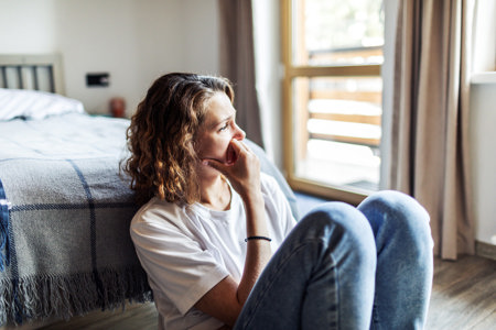 Adult woman with past trauma sitting on the floor next to her bed