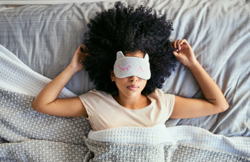 Woman in bed with sensory overload wearing an eye-mask to block migraine-triggering light 