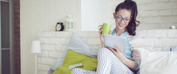 Young woman spending a self-compassionate rest day in bed with hot chocolate and a TV series.