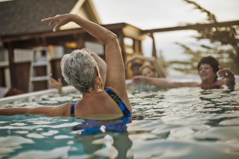A woman in a swimming pool with her arms raised, enjoying the water in swimwear at a leisure centre.